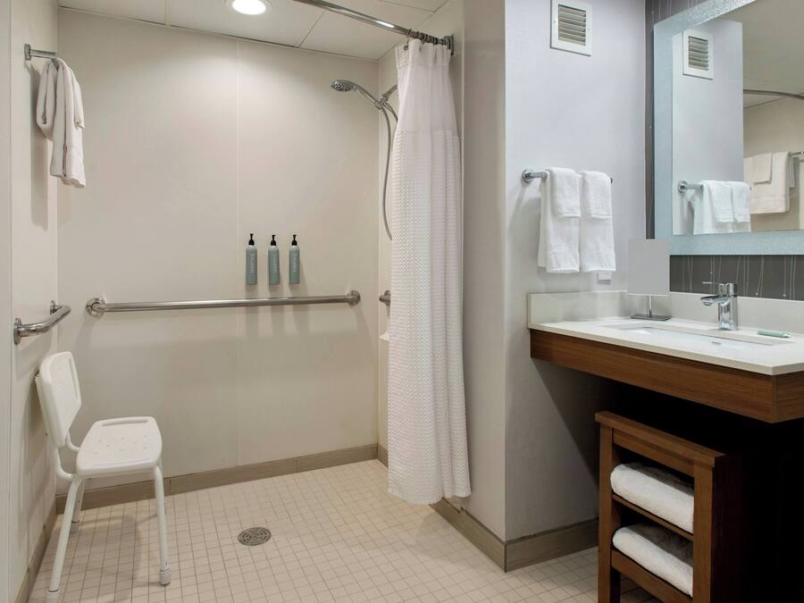 A modern bathroom with a shower, a toilet, a sink, and a chair.