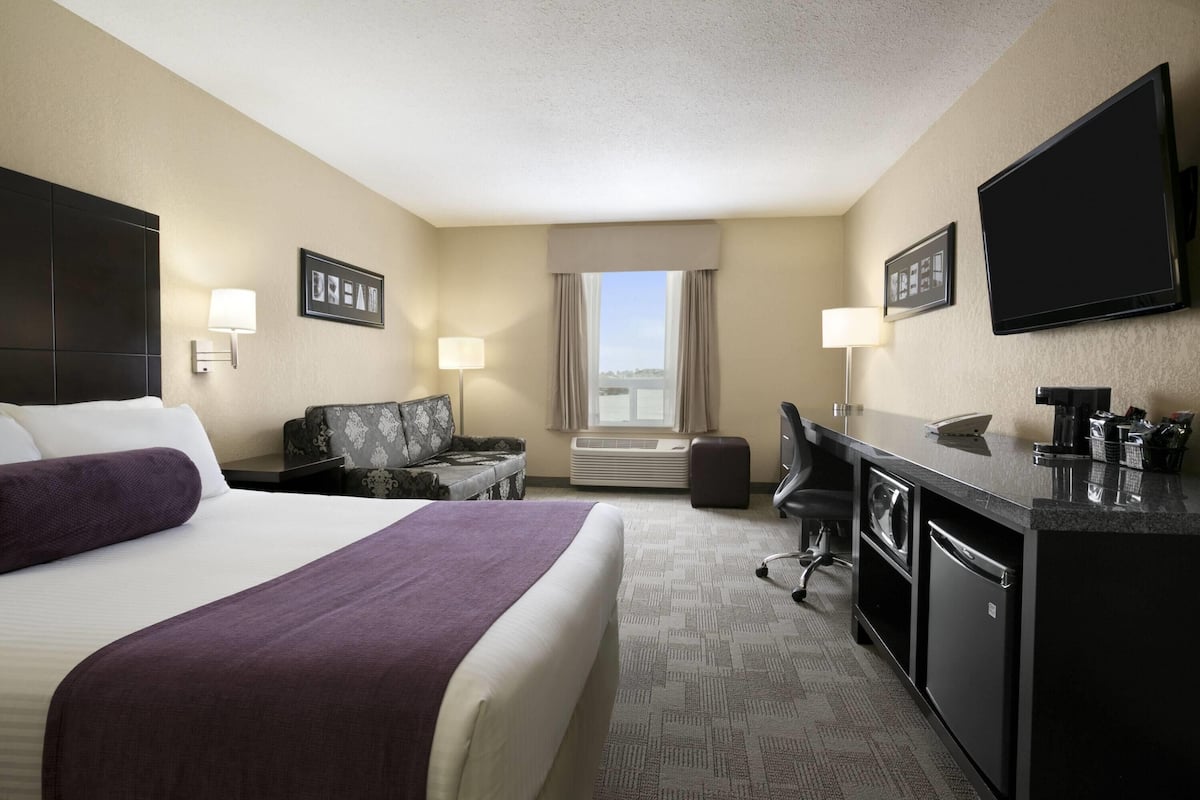 A hotel room with a large bed, a desk with a computer, a chair, a couch, and a TV.