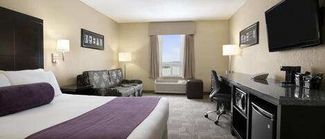 A hotel room with a large bed, a desk with a computer, a chair, a couch, and a TV.