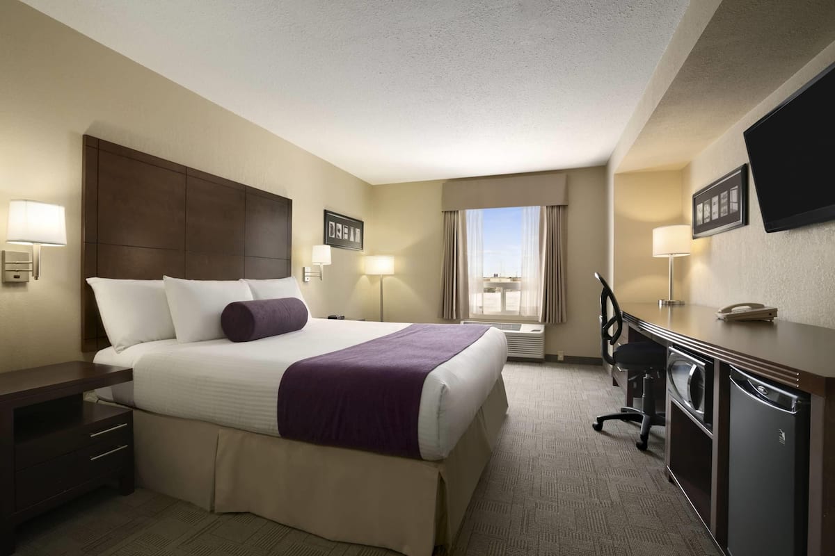 A hotel room with a large bed, a desk, a chair, a TV, and a window with curtains.