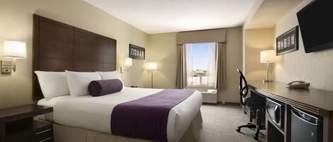 A hotel room with a large bed, a desk, a chair, a TV, and a window with curtains.