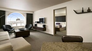 A modern hotel room with a large window, a flat-screen TV, a sofa, a coffee table, and a dining area. - Days Inn by Wyndham Regina (Regina)