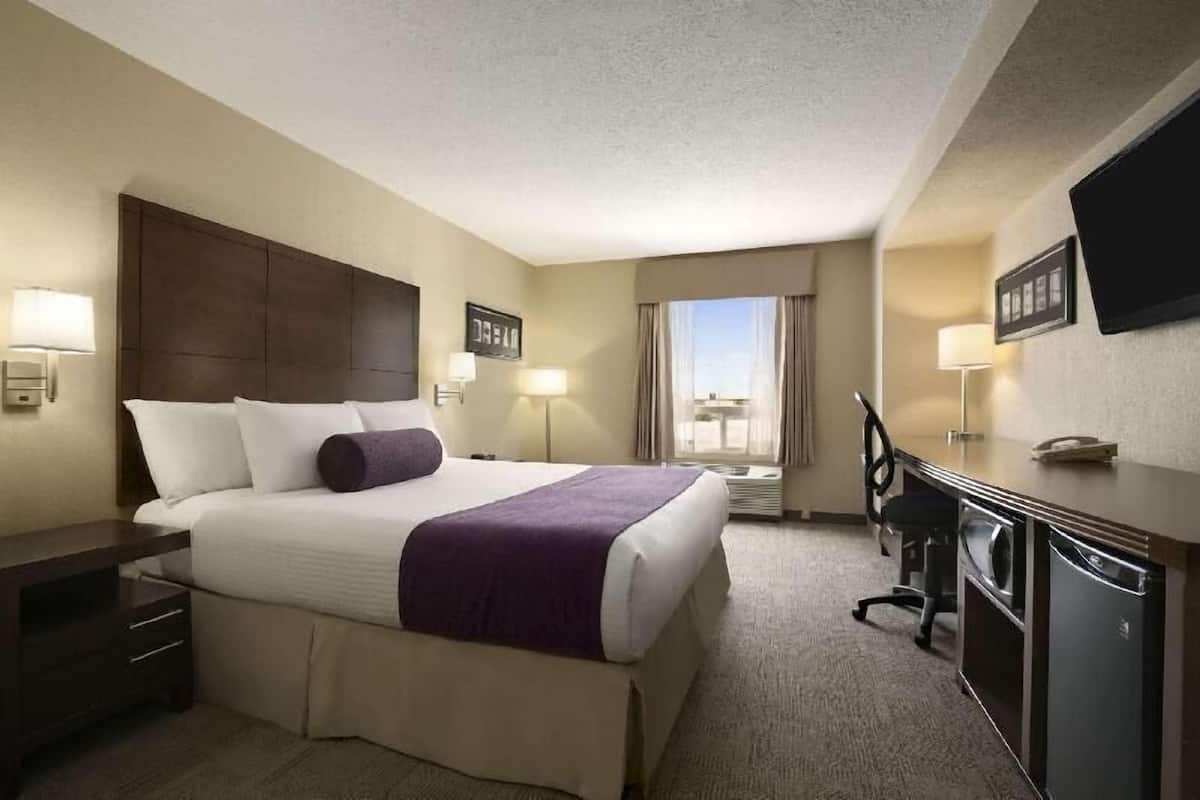 A hotel room with a bed, desk, chair, TV, and window.