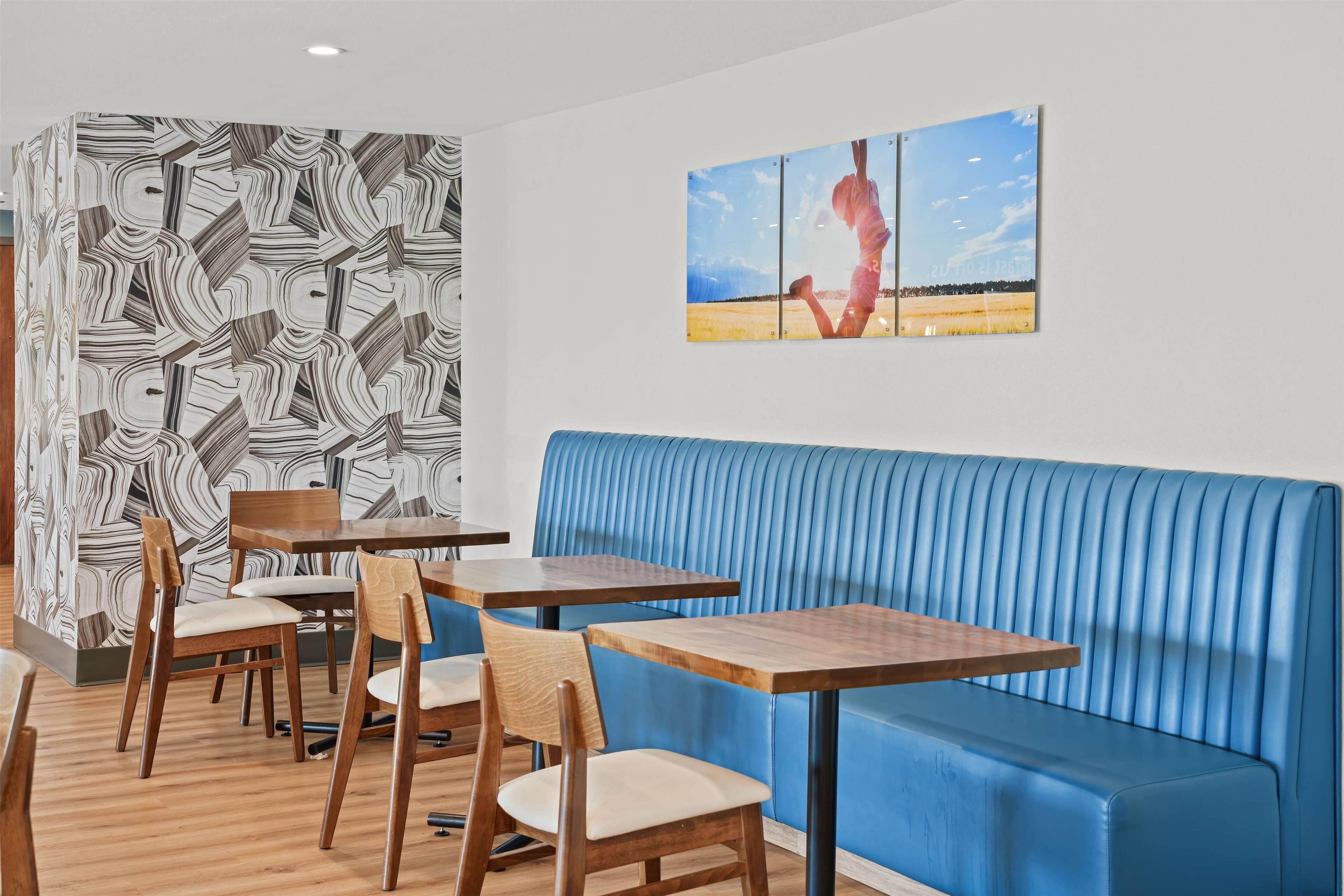 Un restaurante con mesas y sillas de madera, un banco acolchado azul y una pared con un diseño geométrico.