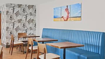 Un restaurante con mesas y sillas de madera, un banco acolchado azul y una pared con un diseño geométrico.