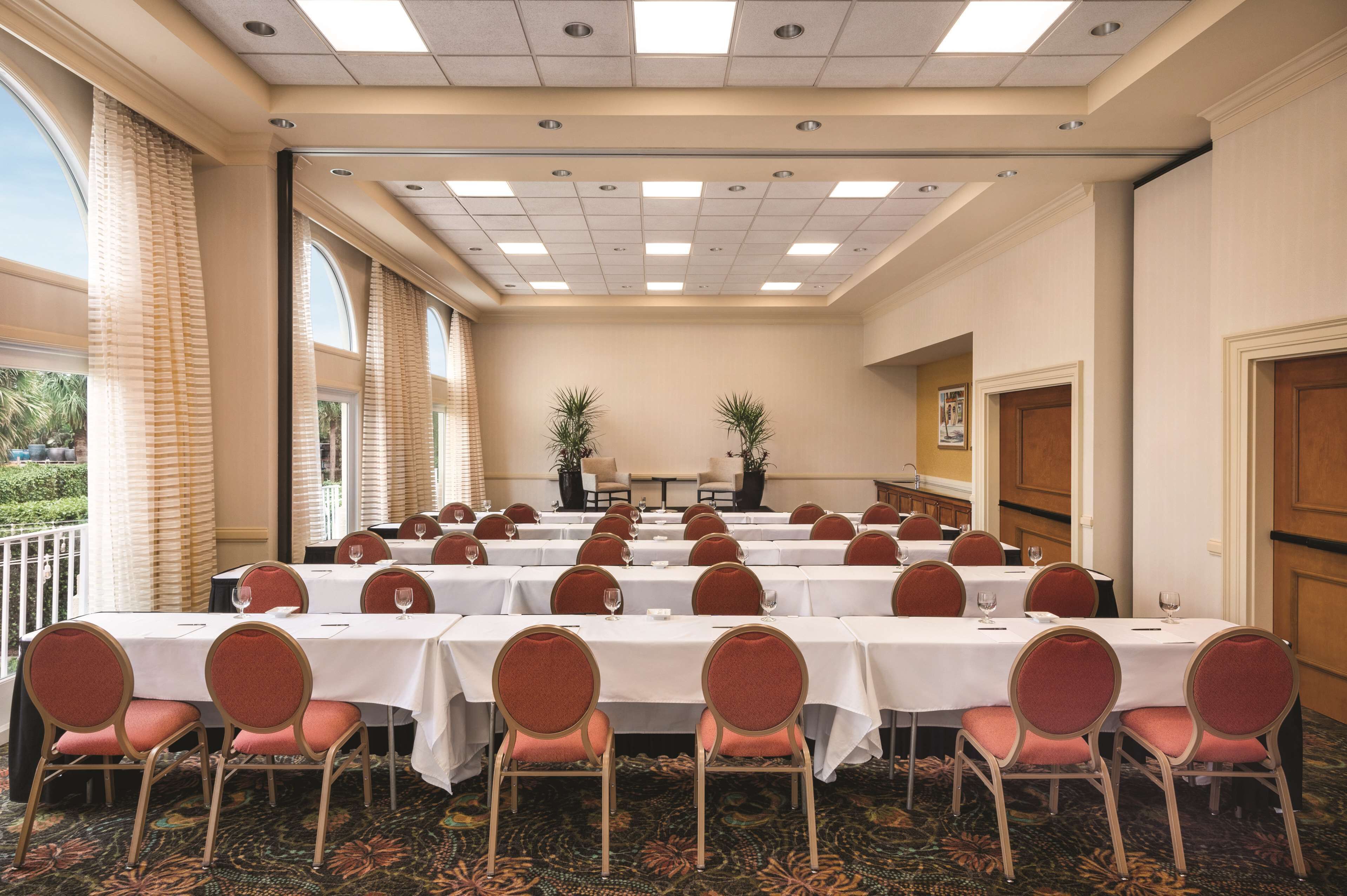 Un salón de conferencias con varias mesas y sillas, ventanas amplias e iluminación empotrada en el techo.