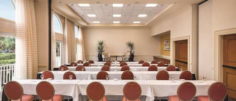 Un salón de conferencias con varias mesas y sillas, ventanas amplias e iluminación empotrada en el techo.