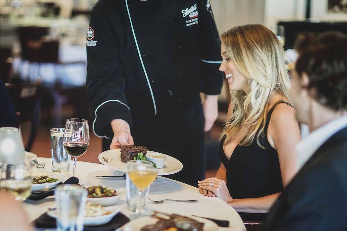 A restaurant setting with a waiter serving a dish to a seated guest.