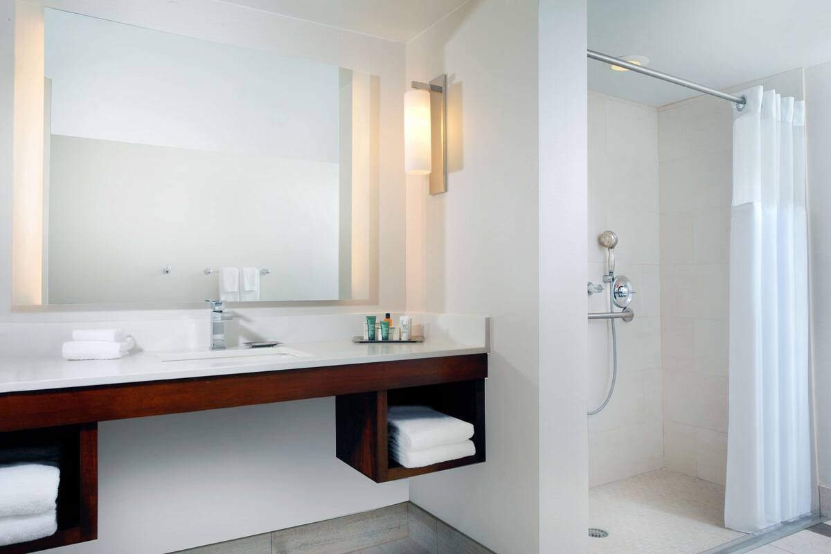 Une salle de bain moderne avec un grand miroir, un meuble-lavabo en bois, une douche avec une porte en verre et un porte-serviettes.