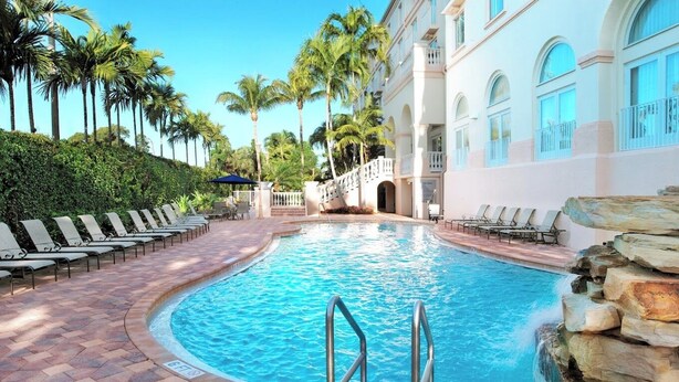 A swimming pool with lounge chairs and palm trees.