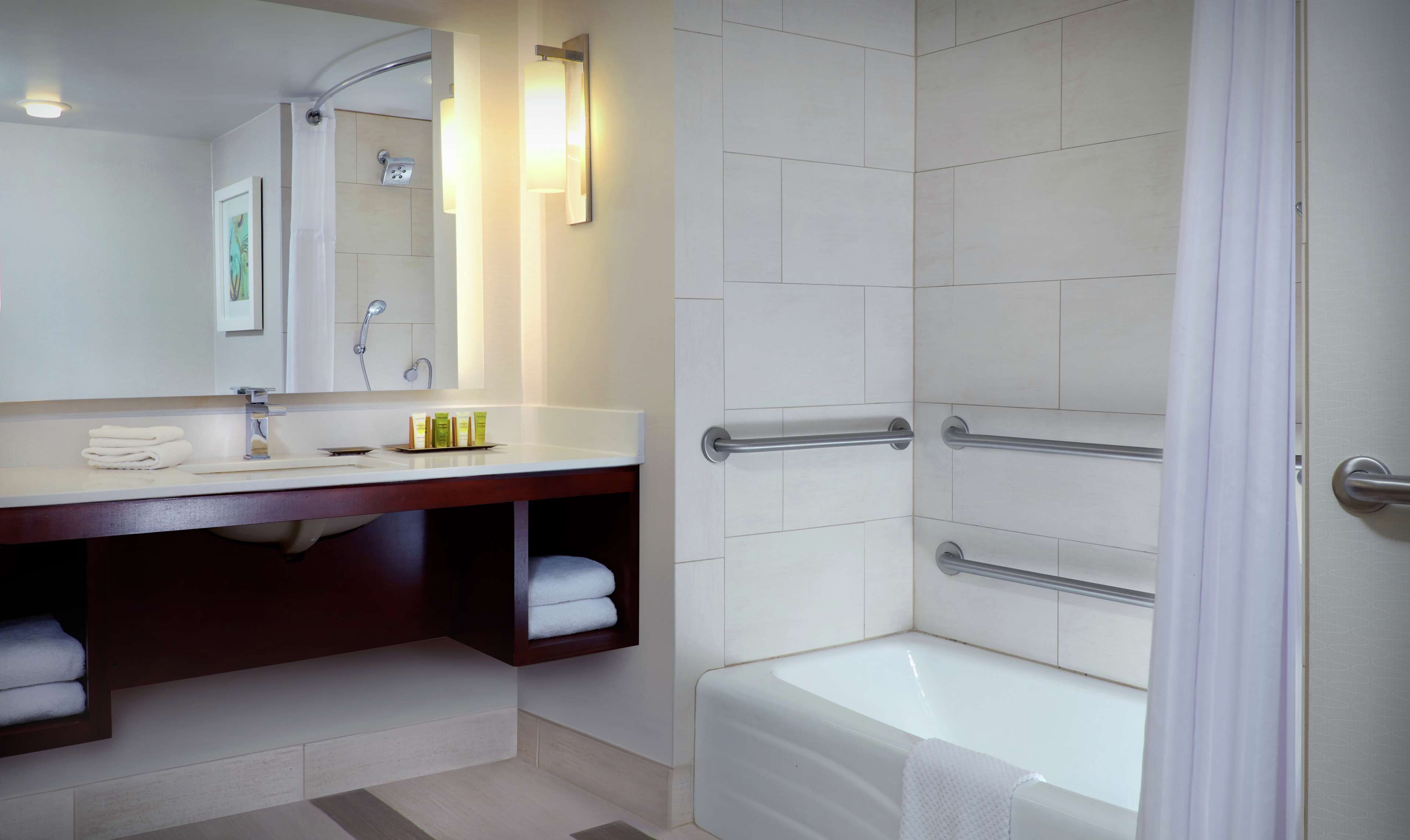 Une salle de bain moderne équipée d’un meuble-lavabo, d’une douche avec des barres d’appui et d’une baignoire.