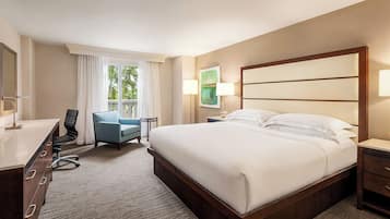 Quarto de hotel com cama, escrivaninha, cadeira e janela com cortinas.