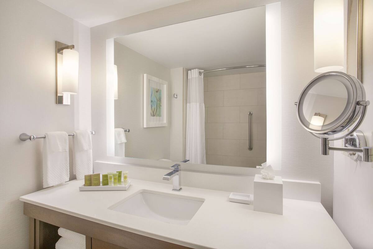 Une salle de bain moderne avec un grand miroir, un lavabo et un espace douche.
