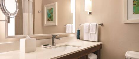 A modern bathroom with a large mirror, a sink, a toilet, and a framed artwork on the wall.