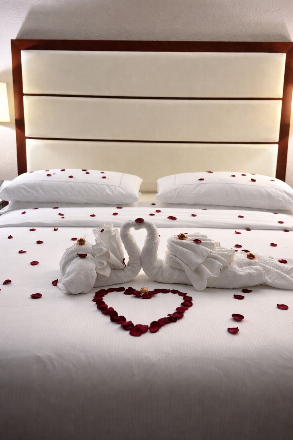 A bed with white linens, two pillows, and a heart-shaped arrangement of rose petals.