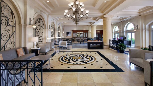 A spacious lobby with a central chandelier, seating areas, and a large decorative rug. - Hilton Naples (Naples)