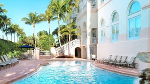A swimming pool with a stone waterfall feature, surrounded by lounge chairs and palm trees. - Hilton Naples (Naples)