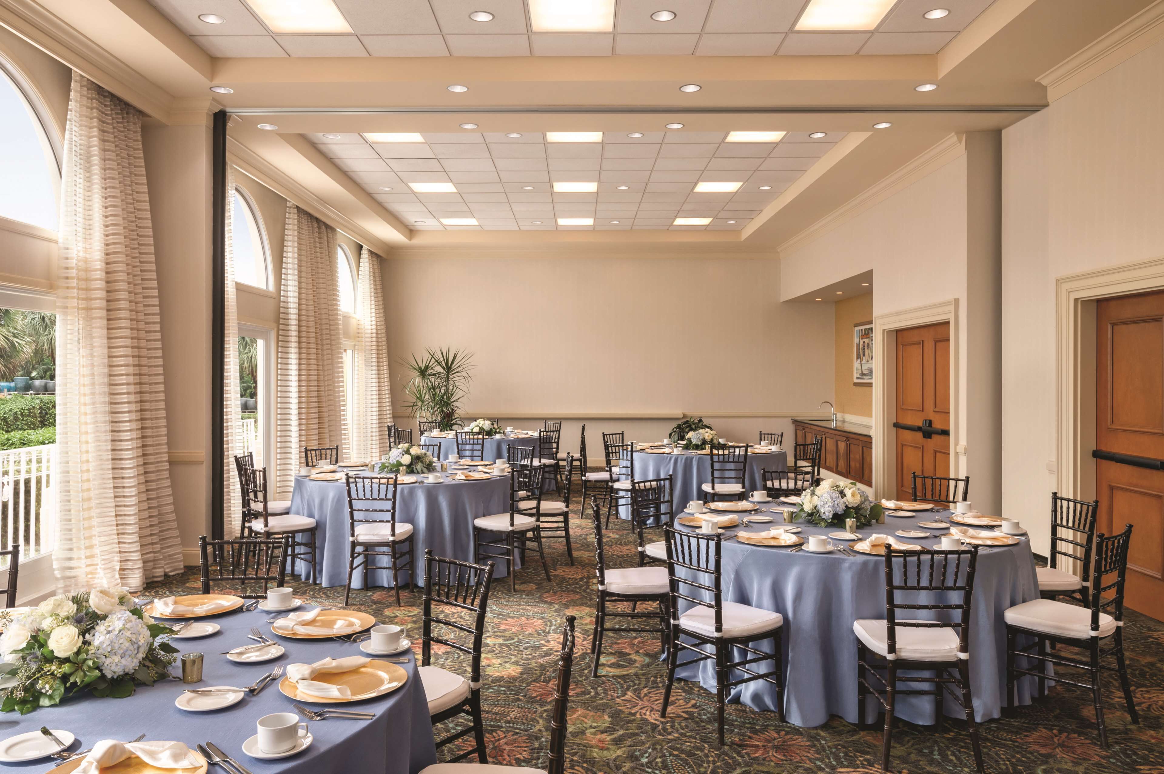 A banquet hall with round tables set for dining, featuring floral centerpieces and a carpeted floor.