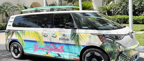 Un autobús lanzadera para la playa con un diseño tropical colorido, que muestra la marca 'Hilton Naples Beach Shuttle'.