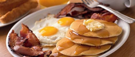 Ein Teller mit Eiern, Speck, Pfannkuchen, Butter und Sirup.