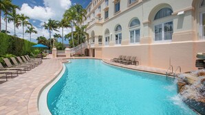 A swimming pool with lounge chairs, palm trees, and a building with arched windows.