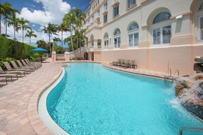 A swimming pool with lounge chairs, palm trees, and a building with arched windows.