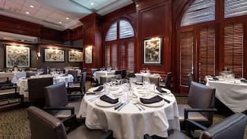 A formal dining area with round tables set for multiple guests, featuring white tablecloths and silverware.