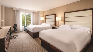 A hotel room with two beds, a desk, a chair, and a window with curtains.