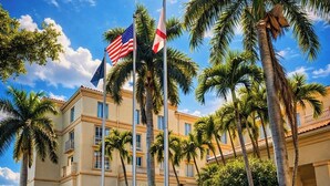 A hotel with a symmetrical facade, palm trees, and two flags. - Hilton Naples (Naples)