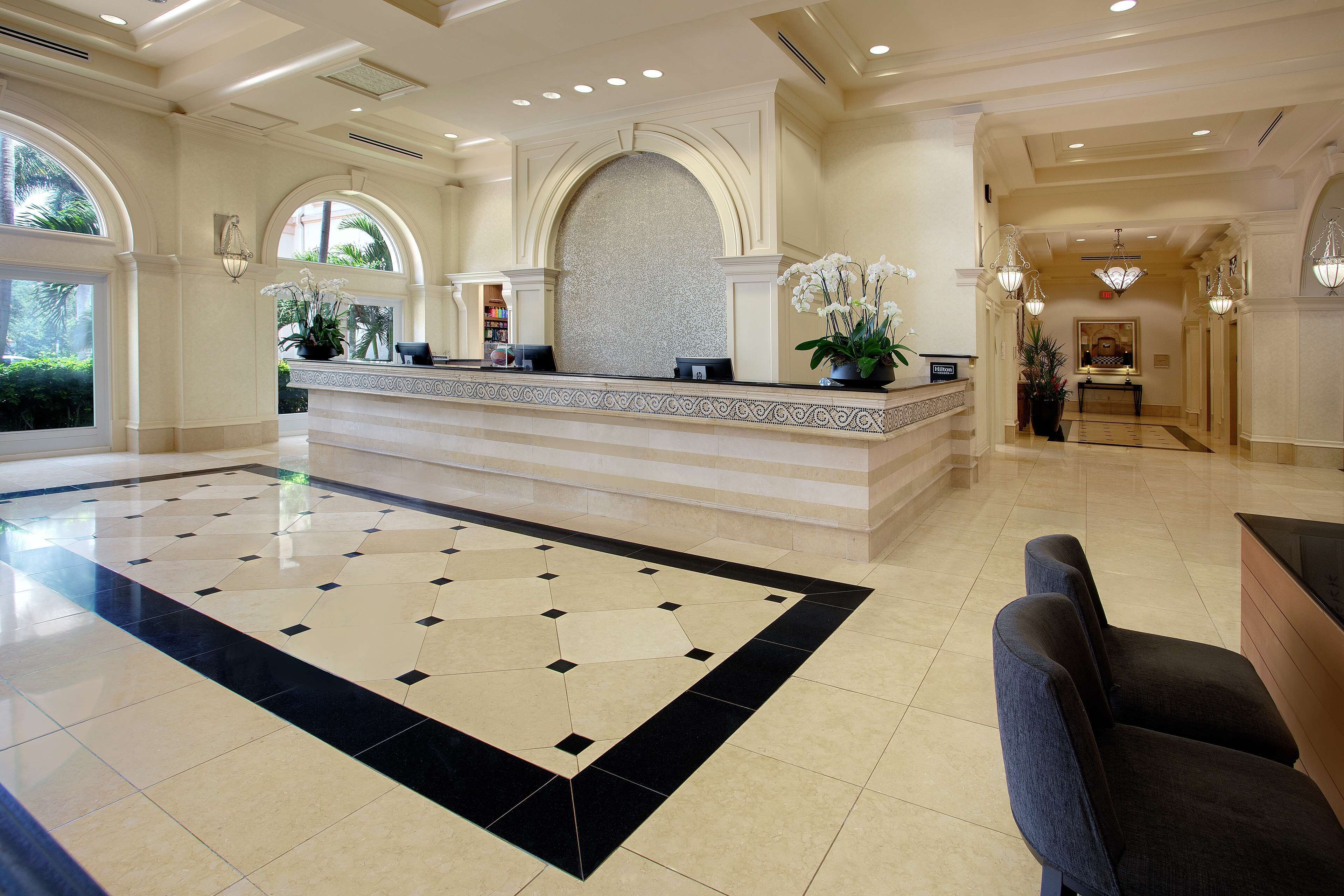 A spacious lobby with a reception desk, a patterned floor, and a view of the outdoors through large windows.
