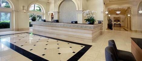 A spacious lobby with a reception desk, a patterned floor, and a view of the outdoors through large windows.