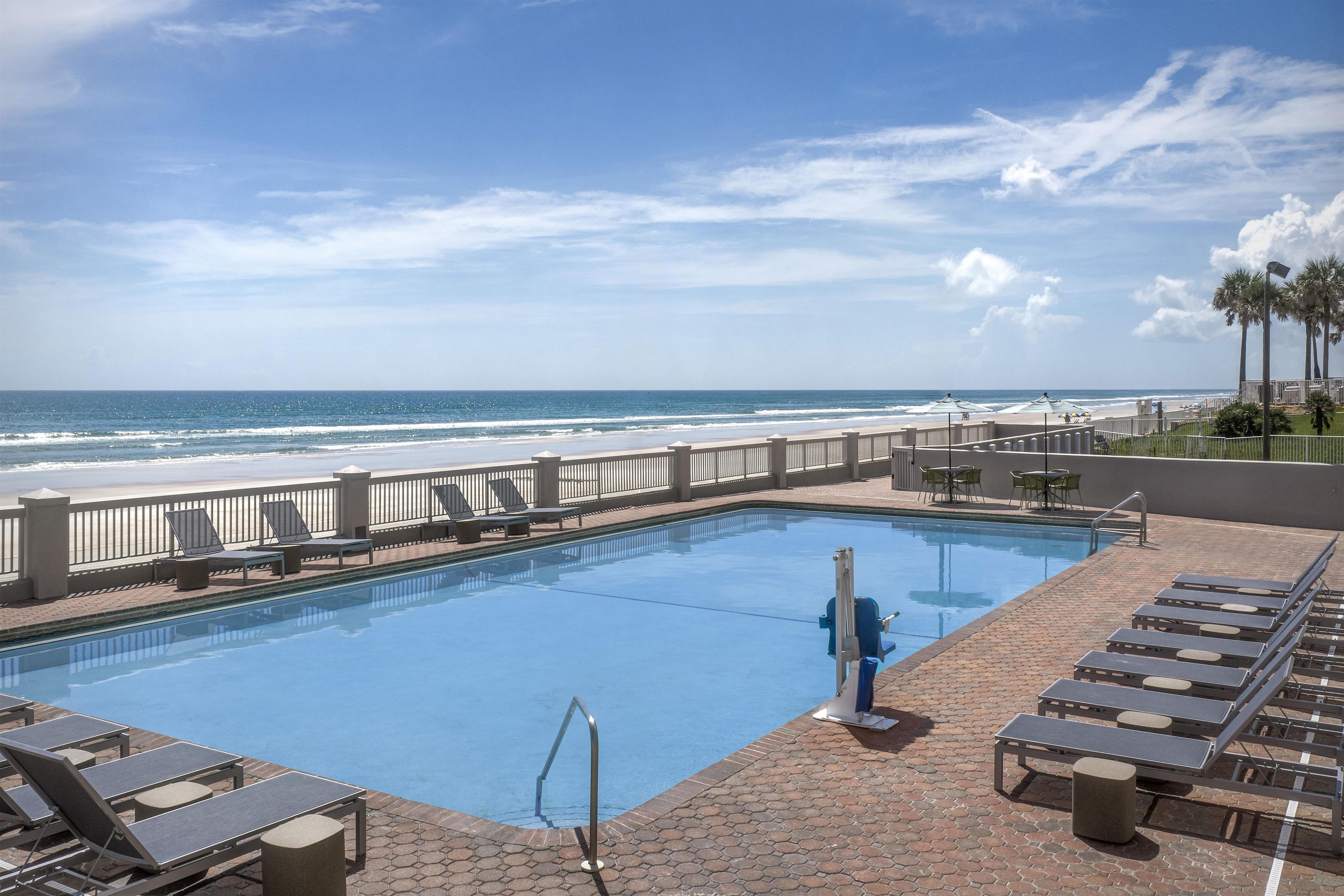 A swimming pool with a view of the ocean, lounge chairs, and a palm tree.