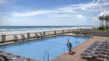 A swimming pool with a view of the ocean, lounge chairs, and a palm tree.