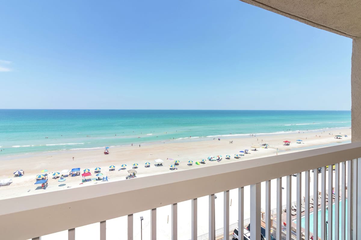 A beach view from a balcony with a pool and beach umbrellas.