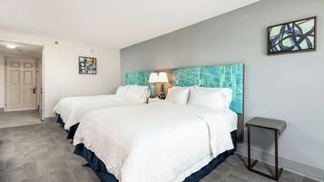 A hotel room with two beds, a nightstand with a lamp, and artwork on the walls.