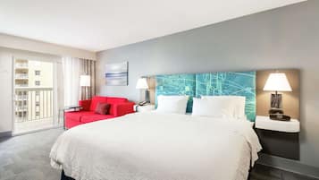 A hotel room with a large bed, a red sofa, a wall-mounted lamp, and a view of the outside balcony.