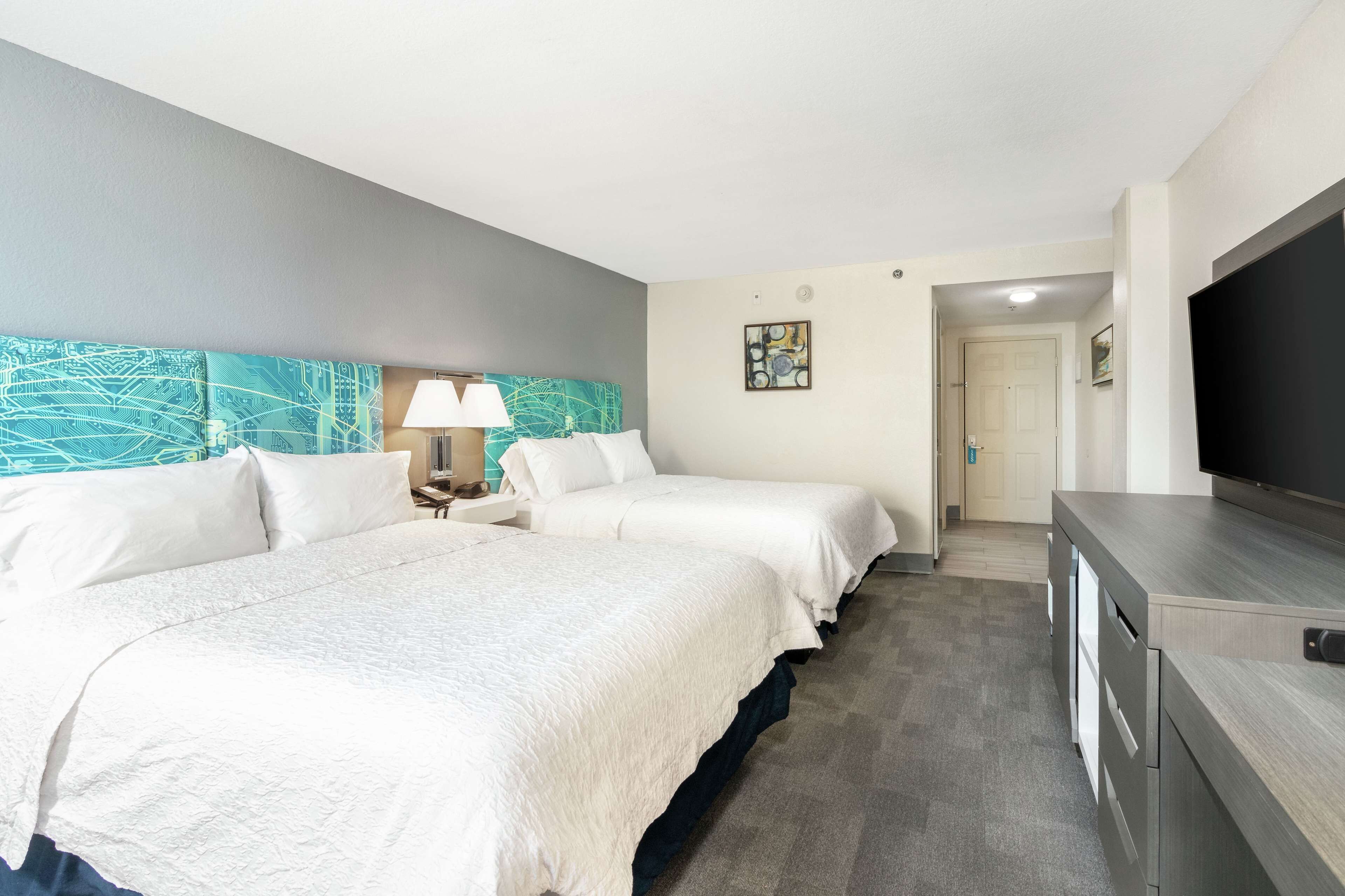 Habitación de hotel con dos camas, televisión, escritorio y puerta que da al baño.