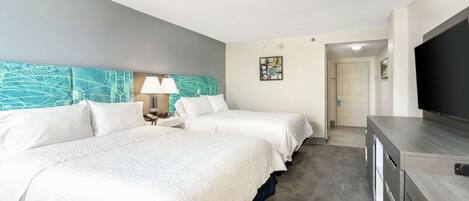 Habitación de hotel con dos camas, televisión, escritorio y puerta que da al baño.
