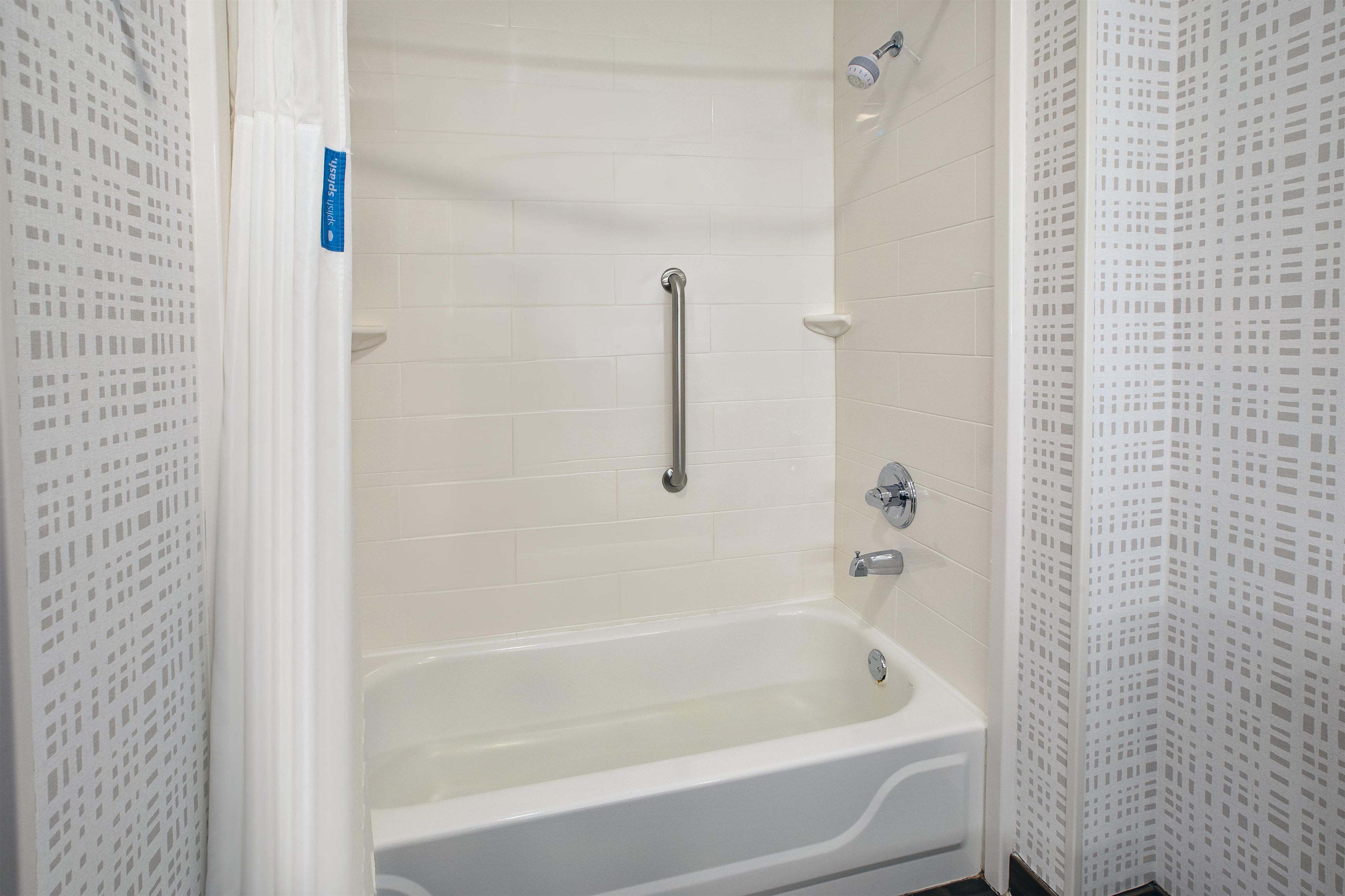 A bathroom with a white bathtub, a handheld showerhead, and a grab bar.