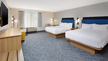A hotel room with two beds, a desk, a chair, a TV, and a window with curtains.