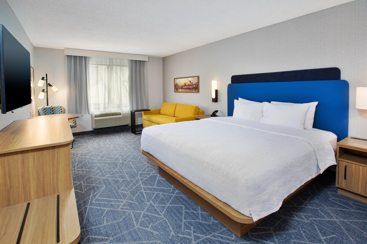 A hotel room with a large bed, a desk, a chair, and a television.