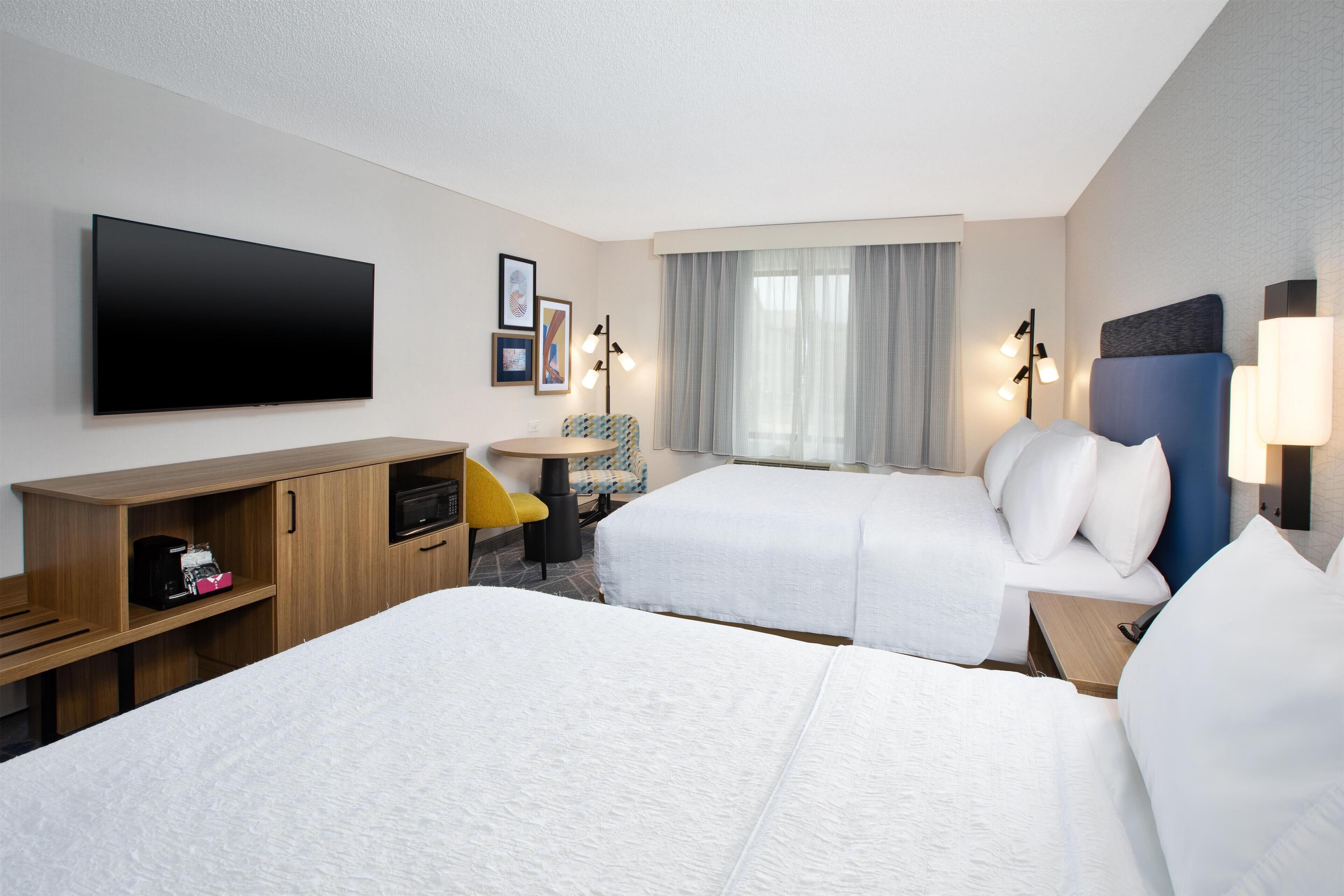 A hotel room with two beds, a TV, a desk, and a chair.