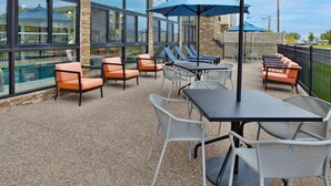 An outdoor patio area with seating arrangements, including chairs and tables, and large umbrellas providing shade. - Hampton Inn Hotel Detroit/Belleville-Airport Area (Belleville)