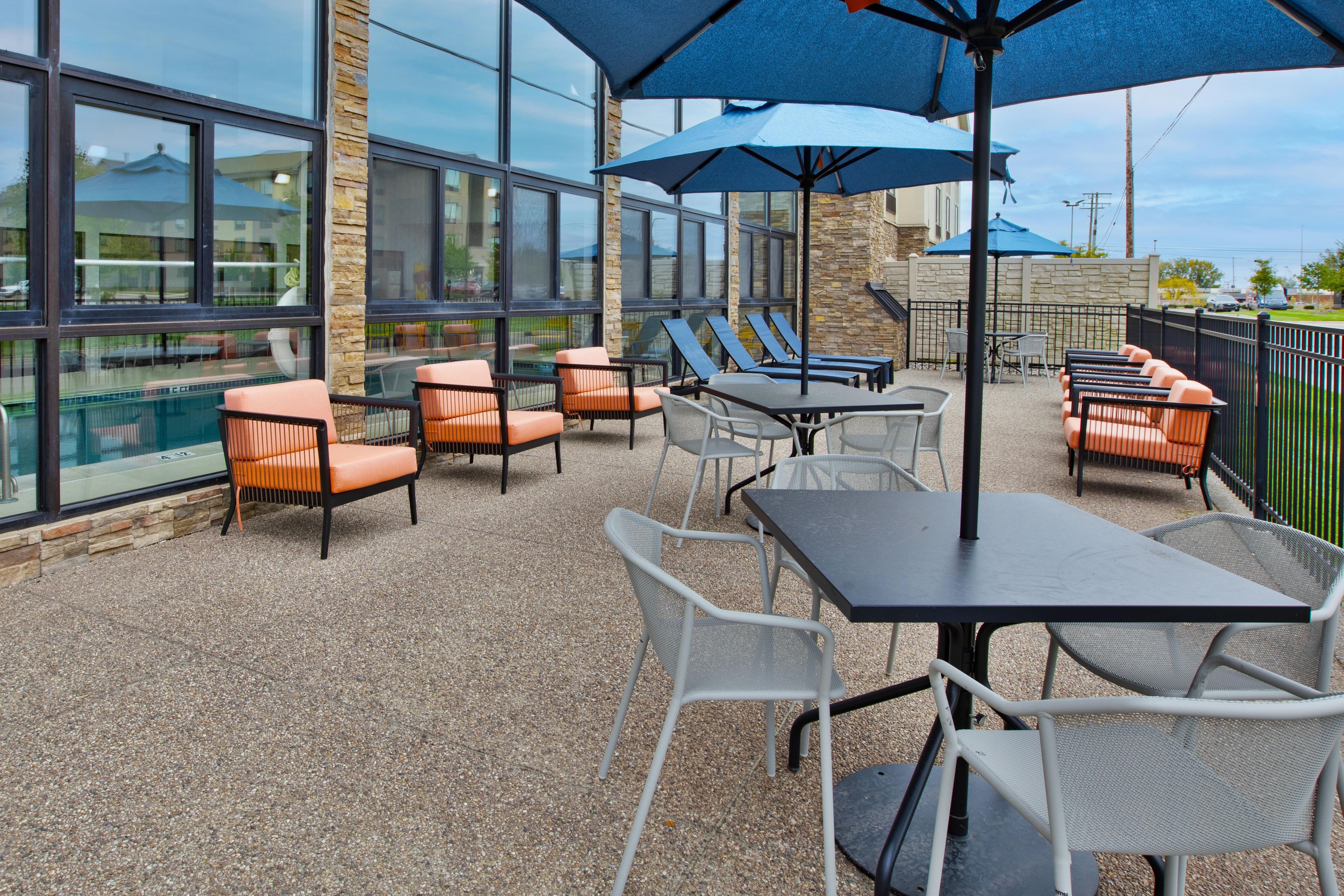 An outdoor patio with seating and umbrellas, large windows, and a stone wall.