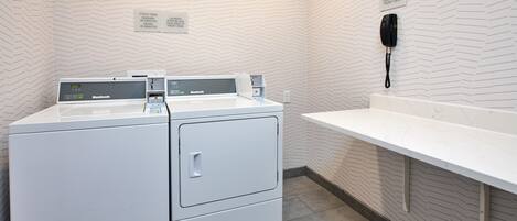 A laundry area with a white wall, a white counter, and a phone mounted on the wall.