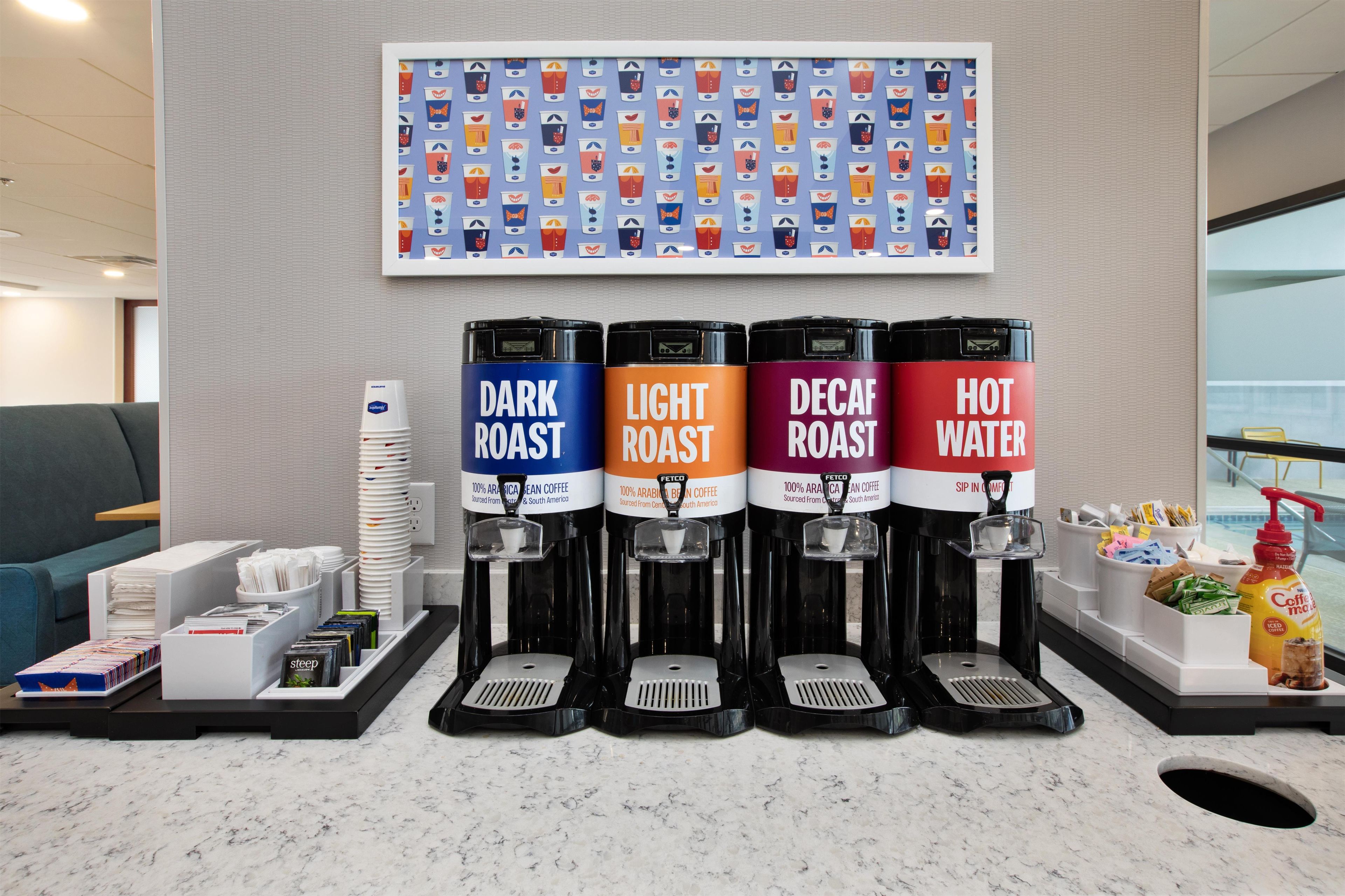 A coffee station with four dispensers labeled DARK ROAST, LIGHT ROAST, DECAF ROAST, and HOT WATER.