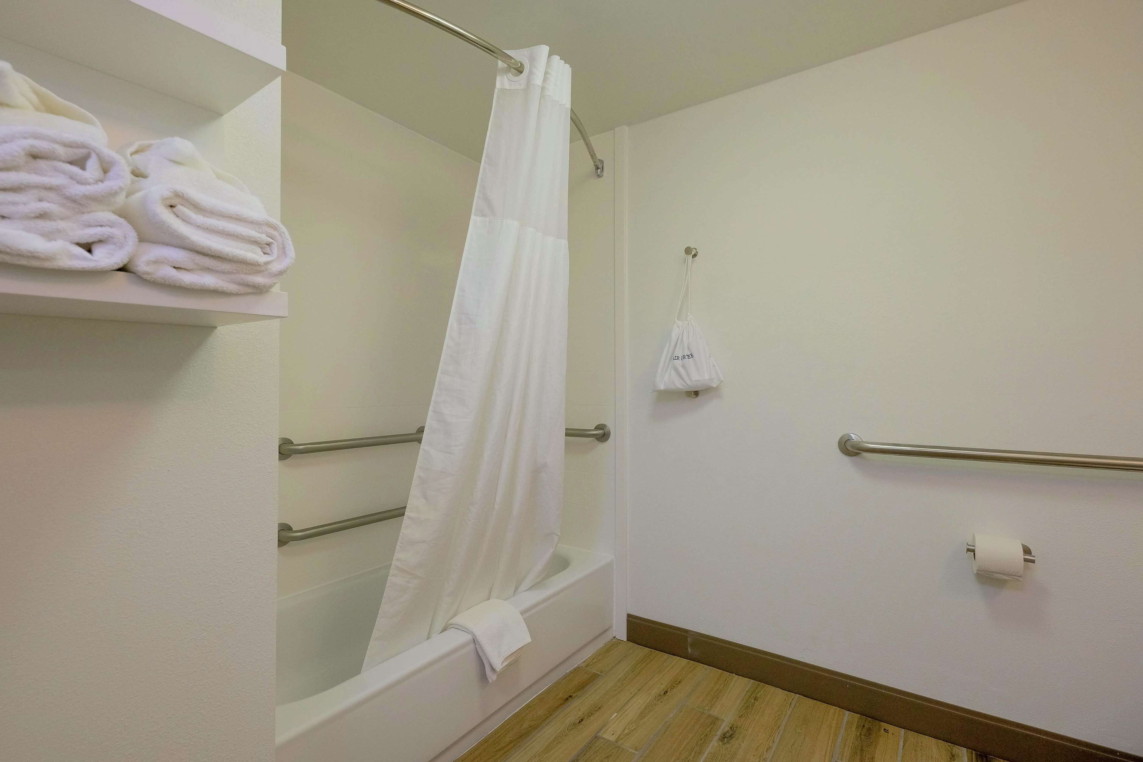 Une salle de bain équipée d’une baignoire, d’un rideau de douche, d’un porte-serviettes avec des serviettes, d’une barre d’appui et d’un porte-rouleau de papier toilette.