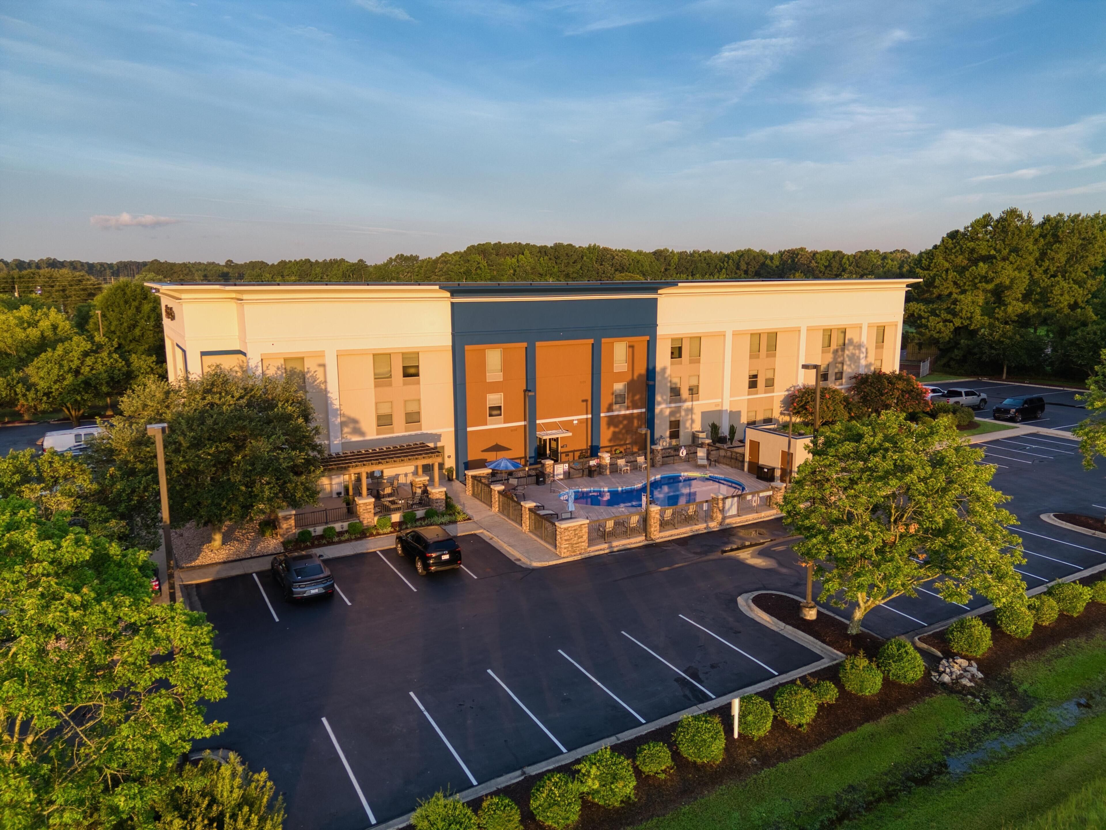 A hotel with a swimming pool, outdoor seating, and a parking lot.