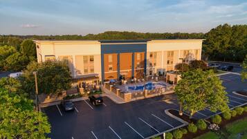 A hotel with a swimming pool, outdoor seating, and a parking lot.