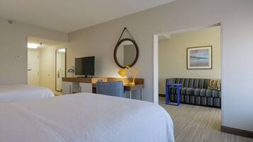 A hotel room with two beds, a desk with a computer and lamp, a sofa, and a framed picture on the wall.